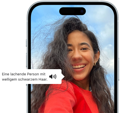 Ein iPhone 15 mit dem Feature VoiceOver, das eine Bildbeschreibung liefert: lachende Person mit welligem schwarzem Haar