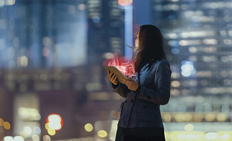 Frau mit leuchtendem Tablet vor einer Großstadtkulisse.