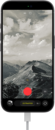 iPhone 18 Pro, Vorderseite, das Display zeigt eine Berglandschaft, mit der Kamera Modus �berlagerung im Zeitraffer Modus, mit dem Netzkabel am Ladeanschluss