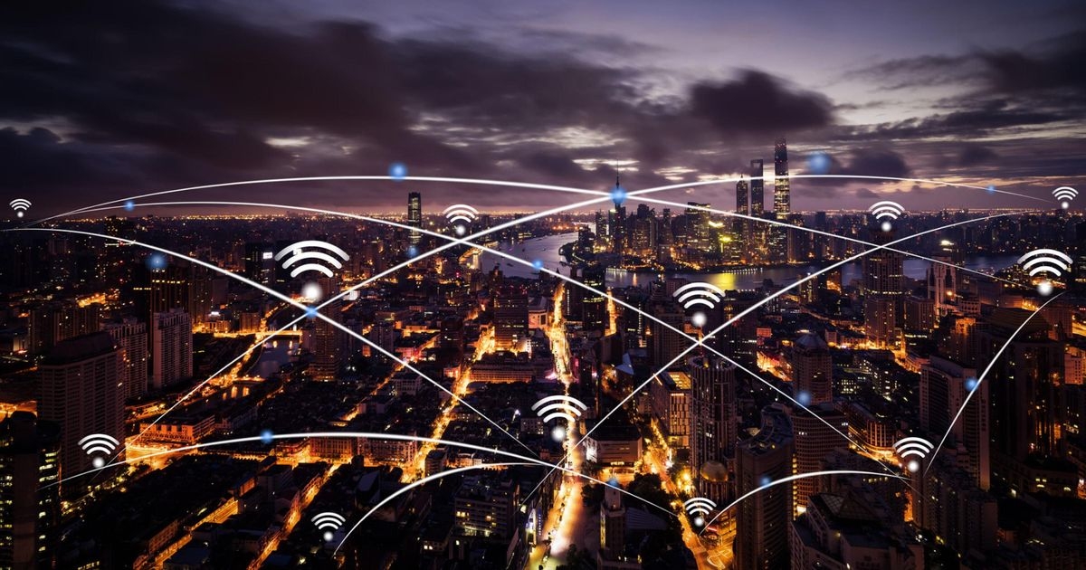 Nächtliche Ansicht einer Großstadt. Über einzelnen Gebäuden sind Netzwerksymbole und sie sind durch weiße Linien miteinander verbunden.