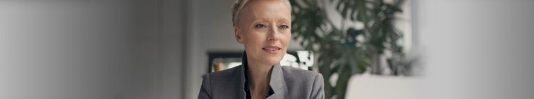 Frau mit kurzen hellen Haaren im grauen Blazer im Büro