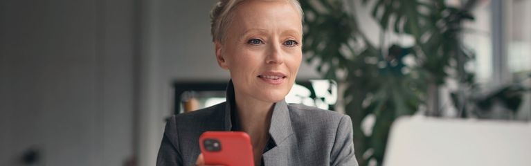 Junge Dame am Schreibtisch mit Laptop und rotem Handy