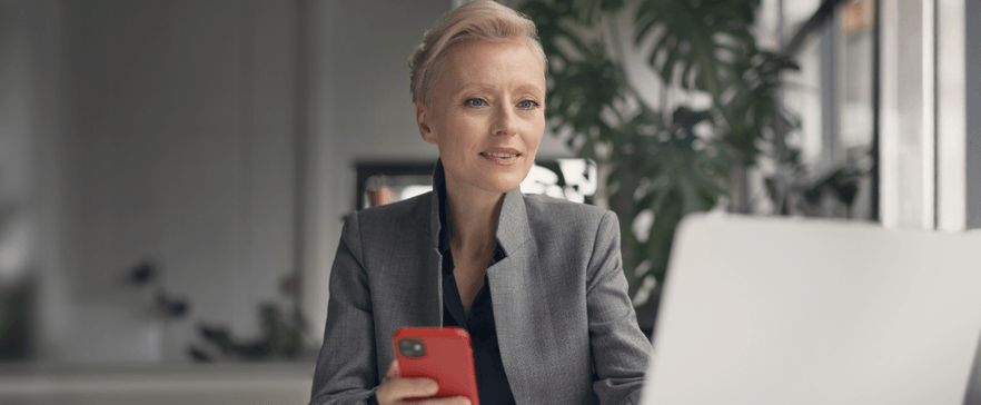 Geschäftsfrau sitzt mit Handy vor dem Laptop