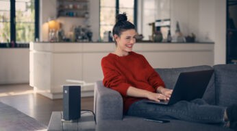 Frau sitzt auf Couch mit Laptop und neben ihr steht ein Router