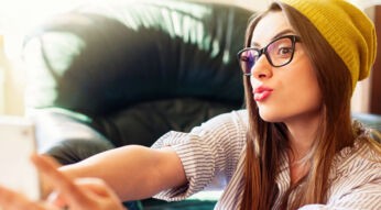 Frau mit gelber Mütze schießt mit dem Smartphone ein Selfie von sich.