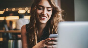 Was ist Galaxy Store? Junge Frau sitzt am Tisch und schaut auf ihr Smartphone.