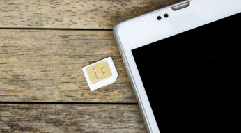 SIM-Karte liegt neben einem weißen Smartphone auf einem Holztisch.