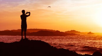 Junger Mann macht mit seinem Smartphone ein Foto vom Sonnenuntergang.