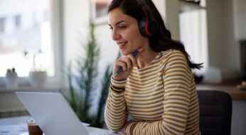 Eine junge Frau arbeitet an einem Laptop und nutzt ein kabelloses Headset