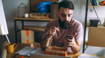 Junger Mann sitzt mit Smartphone an seinem Schreibtisch