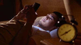 Mann mit Smartphone und Wecker