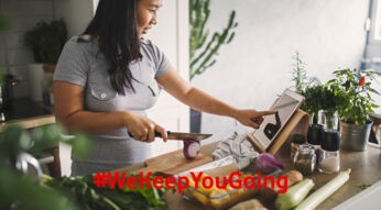 Eine Frau schneidet Gemüse in der Küche und nutzt ihr Tablet, um ein Gericht per Anleitung zuzubereiten.