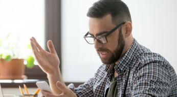 Mann schaut wütend auf sein Smartphone.