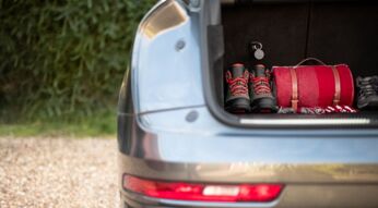 Im Kofferraum eines Autos liegen Wanderschuhe und ein Rucksack, befestigt daran ist der Curve GPS-Tracker von Vodafone.