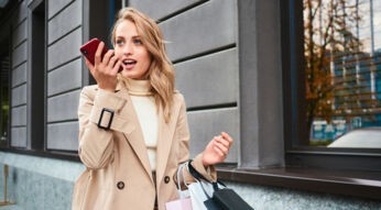 Frau mit Einkaufstüten spricht einen Kurzbefehl für Siri ins iPhone