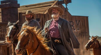 Im Artikel zu den besten Western-Serien siehst du ein Bild aus der Serie Godless ist Jeff Daniels als Frank Griffin. Er reitet auf einem braunen Pferd durch eine staubige Westernstadt, begleitet von einem weiteren Reiter