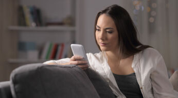 Frau sitzt mit Smartphone auf der Couch