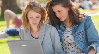 Zwei Frauen im Park gucken auf einen Laptop-Bildschirm