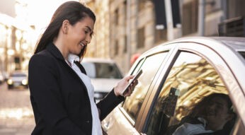 Frau öffnet Tür eines Autos, während sie ihr Smartphone in der Hand hält.
