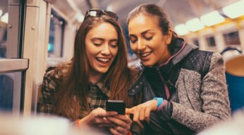 Zwei junge Frauen in der Bahn schauen gemeinsam auf ein Smartphone