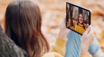 Junge Frau sitzt im Herbst im Park und macht Selfie mit dem iPad Pro 2021