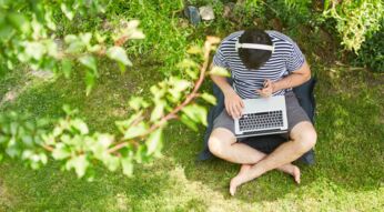 Ein Mann mit Kopfhörer und Laptop sitzt im Grünen.