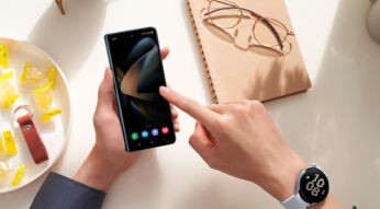 Linke Hand hält Galaxy Z Fold4 über Tisch, rechte Hand tippt auf Display
