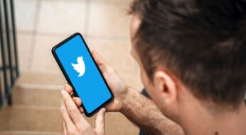 Twitter-Logo auf einem Smartphone, gehalten von einem jungen Mann