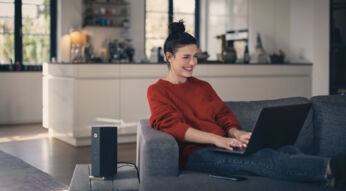 Frau sitzt auf Sofa mit Laptop und Kabelrouter von Vodafone steht auf dem Tisch