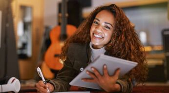 Eine Frau hält ein iPad in der Hand und macht sich Notizen auf einem Block