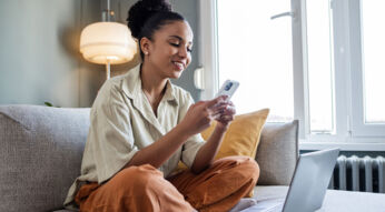 Frau sitzt auf dem Sofa und unternimmt Einstellungen zur Datensicherung an ihrem Smartphone