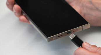 rechte Hand hält ein Galaxy S24 Ultra vor einem weißen Hintergrund, die linke Hand hält ein USB-Kabel