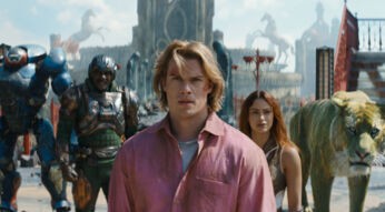 Im Bild zum Masters of the Universe neuer Film ist Adam, gespielt von Nicholas Galitzine, im Vordergrund mit entschlossenem Blick zu sehen. Hinter ihm stehen Teela (Camila Mendes), Man-At-Arms (Idris Elba), Roboto (Kristen Wiig) und der grüne Tiger Cringer. Die Szene wirkt episch und angespannt, mit einer fantasievollen, mittelalterlich-futuristischen Kulisse im Hintergrund.