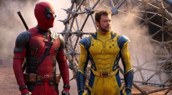 Das Bild zur Deadpool & Wolverine-Kritik zeigt Ryan Reynolds als Deadpool und Hugh Jackman als Wolverine. Beide Charaktere stehen nebeneinander vor einer rauchigen, futuristischen Kulisse, die möglicherweise an ein Schlachtfeld oder eine industrielle Umgebung erinnert. Deadpool (Ryan Reynolds) trägt seinen typischen rot-schwarzen Anzug mit mehreren Taschen und Gürteln sowie sein charakteristisches Schwert auf dem Rücken. Wolverine (Hugh Jackman) ist in einem gelb-blauen Anzug zu sehen, der stark an das klassische Comic-Kostüm des Charakters erinnert. Der Anzug betont seine muskulöse Statur und ist mit einigen metallischen Akzenten versehen. Beide wirken entschlossen und bereit für die nächste Herausforderung, was durch ihre angespannten und konzentrierten Gesichtsausdrücke unterstrichen wird.