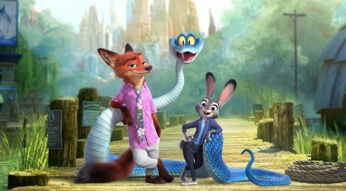 Auf dem Bild zu Zoomania 2 stehen drei tierische Charaktere im Fokus: Ein selbstbewusst wirkender Fuchs in Hawaiihemd, eine fröhlich lächelnde Häsin in Polizeiuniform und eine blaue Schlange mit großen gelben Augen. Die Szenerie spielt auf einem Holzsteg vor grüner Landschaft.