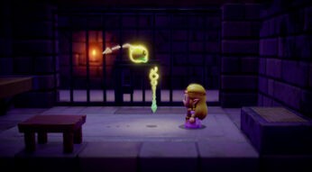 Auf dem Bild zu "Zelda: Echoes of Wisdom Tipps" ist Prinzessin Zelda in einer düsteren, steinernen Umgebung zu sehen. Vor ihr schwebt der leuchtende Tri-Sta, ein wichtiger Gegenstand für den Spielfortschritt. Im Hintergrund befinden sich Gitterstäbe und eine brennende Fackel, die die Atmosphäre verstärken. Zelda trägt ein lilafarbenes Kleid und eine goldene Krone, während sie den Tri-Sta konzentriert betrachtet.