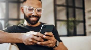 Ein Mann sitzt auf einer Couch und hält ein Handy in der Hand