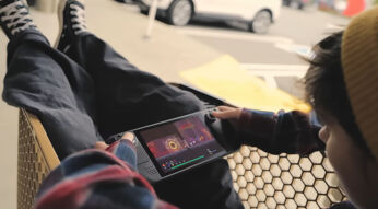 Ein junger Mann sitzt in einem Einkaufswagen und spielt ein Spiel auf einem Steam Deck