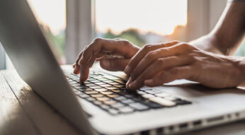 Auf dem Bild in dem Artikel zu den Kosten von ChatGPT im Jahr 2025 sind Hände zu sehen, die auf der Tastatur eines Laptops tippen. Die Szene ist in warmem Tageslicht gehalten, das durch ein Fenster im Hintergrund einfällt, was eine produktive und konzentrierte Atmosphäre vermittelt.
