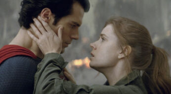 Auf dem Bild zu Superman-Filme Reihenfolge sind Henry Cavill als Superman und Amy Adams als Lois Lane in einer emotionalen Szene zu sehen. Superman trägt sein ikonisches blau-rotes Kostüm, während Lois in einer olivgrünen Jacke gekleidet ist. Sie hält sein Gesicht mit beiden Händen, und beide blicken sich intensiv in die Augen. Im Hintergrund sind Feuer und Rauch zu sehen, was auf eine dramatische Situation hindeutet.