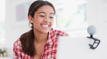 Eine junge Frau schaut in die Webcam, die an ihrem Laptop angebracht ist.