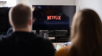 Junges Paar schaut auf einen Fernseher, auf dem das Netflix-Logo abgebildet ist