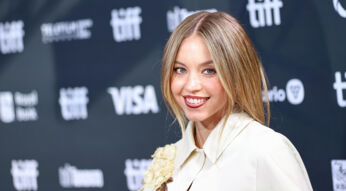 Auf dem Bild in dem Artikel zur möglichen Split Fiction-Verfilmung ist Schauspielerin Sydney Sweeney zu sehen. Sie steht lächelnd vor einer Pressewand und trägt ein elegantes, cremefarbenes Outfit mit floralen Details. Das Bild vermittelt eine positive, glamouröse Stimmung.