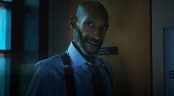 In den GigaTV-Highlights im Juli 2025 siehst du ein Bild aus Final Destination 6: Bloodlines: Tony Todd ist als William John Bludworth zu sehen. Er trägt ein hellblaues Hemd mit Krawatte und Hosenträgern und steht vor einer Tür in dunkler Umgebung.
