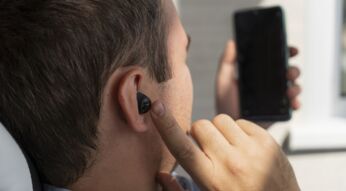 Ein Mann mit In-Ear-Kopfhörern im Ohr schaut auf sein Smartphone