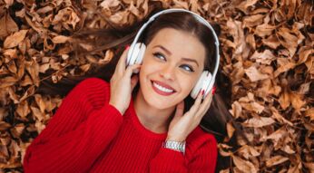 Eine Frau mit Over-Ear-Kopfhörern liegt auf einem Boden inmitten von herabgefallender Herbstblätter.