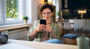Junge Frau sitzt am Tisch und surft auf ihrem Handy.