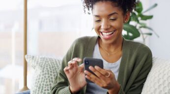 Junge Schwarze Frau schaut lächelnd auf ihr Android-Handy.