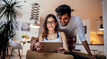 Ein junges Paar schaut gemeinsam auf ein Tablet und lächelt dabei.