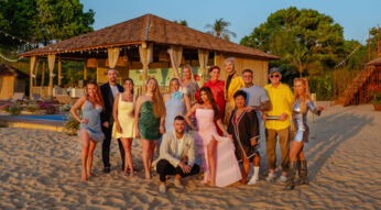 Auf dem Bild zur Show Kampf der RealityAllstars posieren zahlreiche Reality-TV-Persönlichkeiten barfuß am Sandstrand vor einer tropischen Villa. Zu sehen sind u.a. Georgina Fleur, Sandy Fähse, Yeliz Koc, Tayisiya und Yana Morderger, Serkan Yavuz, Kader Loth, Giuliana Farfalla, Kate Merlan, Sam Dylan, Narumol, Paco Herb, Prinz Frédéric von Anhalt und Loona. Die Stimmung wirkt ausgelassen und sommerlich.